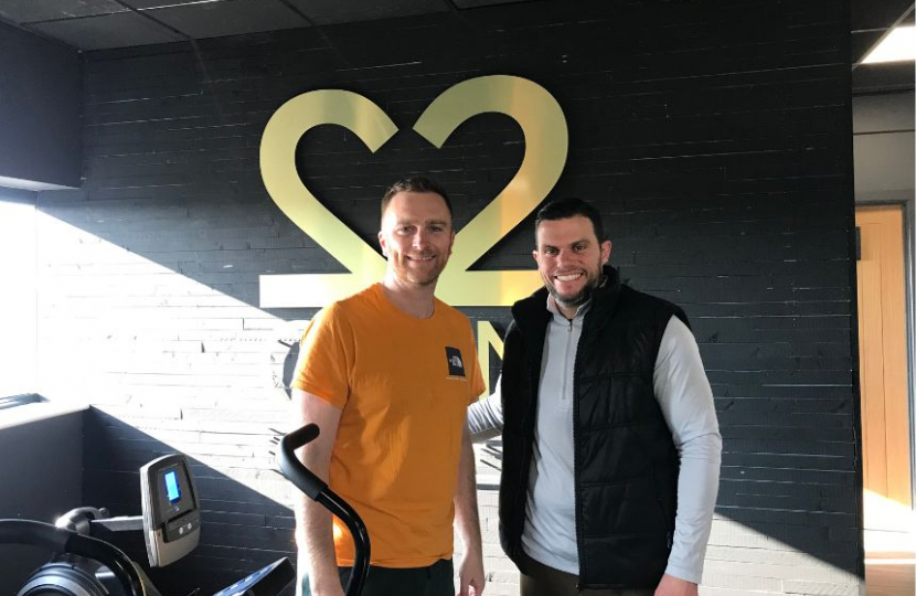 Matt and owner Garry smile in front of the Gyms logo, mounted to the wall behind them.